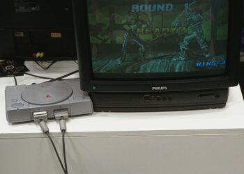 Una console PlayStation 1 è collegata a un televisore a tubo catodico che trasmette l’immagine di due lottatori che combattono in un videogioco della serie Tekken