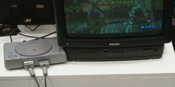 Una console PlayStation 1 è collegata a un televisore a tubo catodico che trasmette l’immagine di due lottatori che combattono in un videogioco della serie Tekken