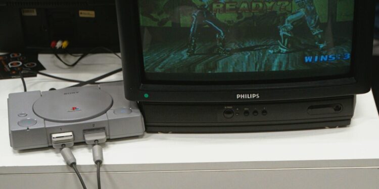 Una console PlayStation 1 è collegata a un televisore a tubo catodico che trasmette l’immagine di due lottatori che combattono in un videogioco della serie Tekken